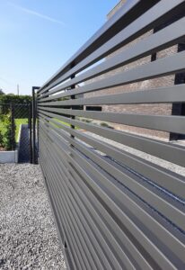 Een metalen poort in zwarte structuurlak met horizontale kokers als afsluiting van een oprit.